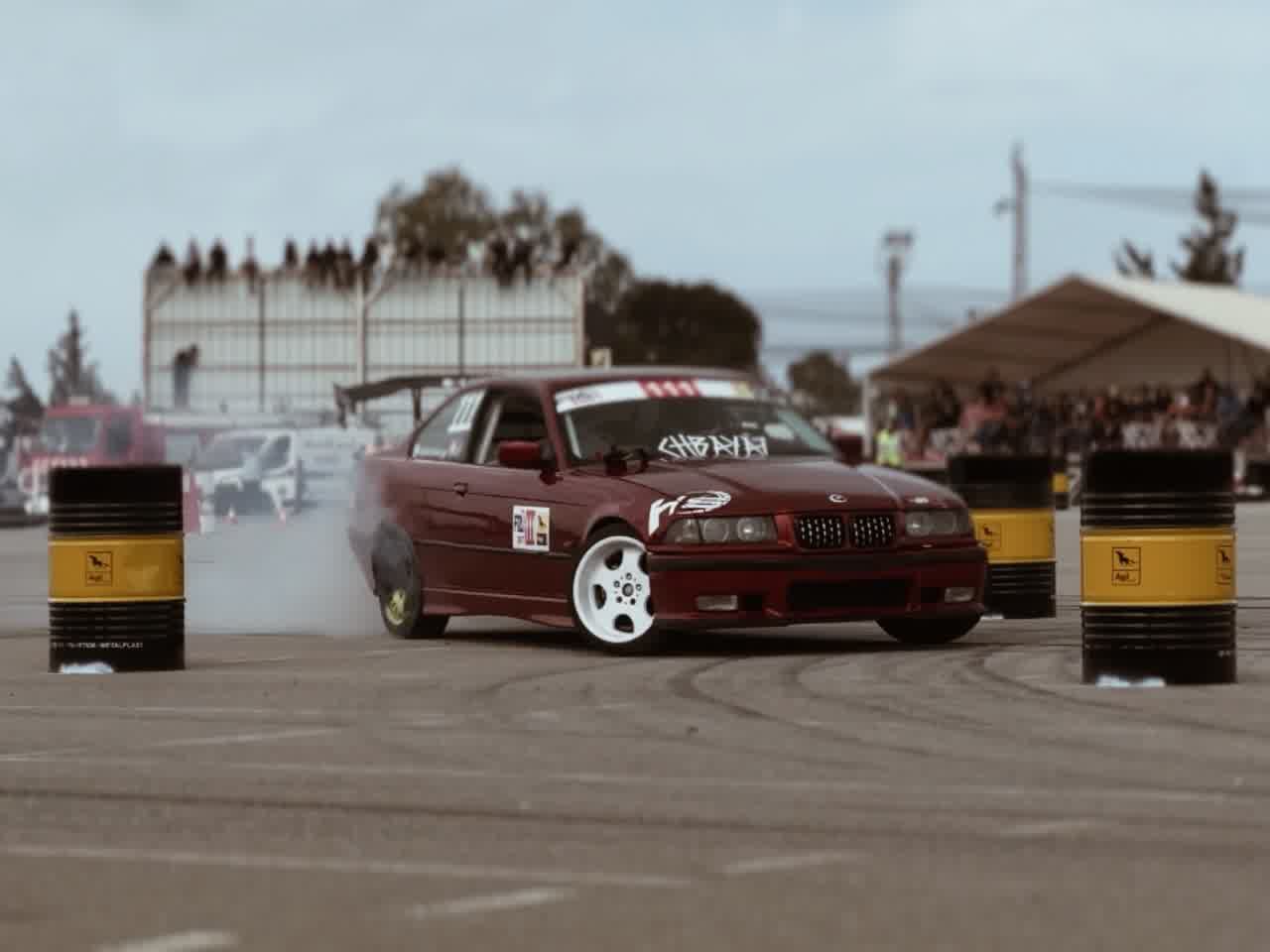 A deep red saloon mid-drift, spectators lining the barrier and the sea behind them.