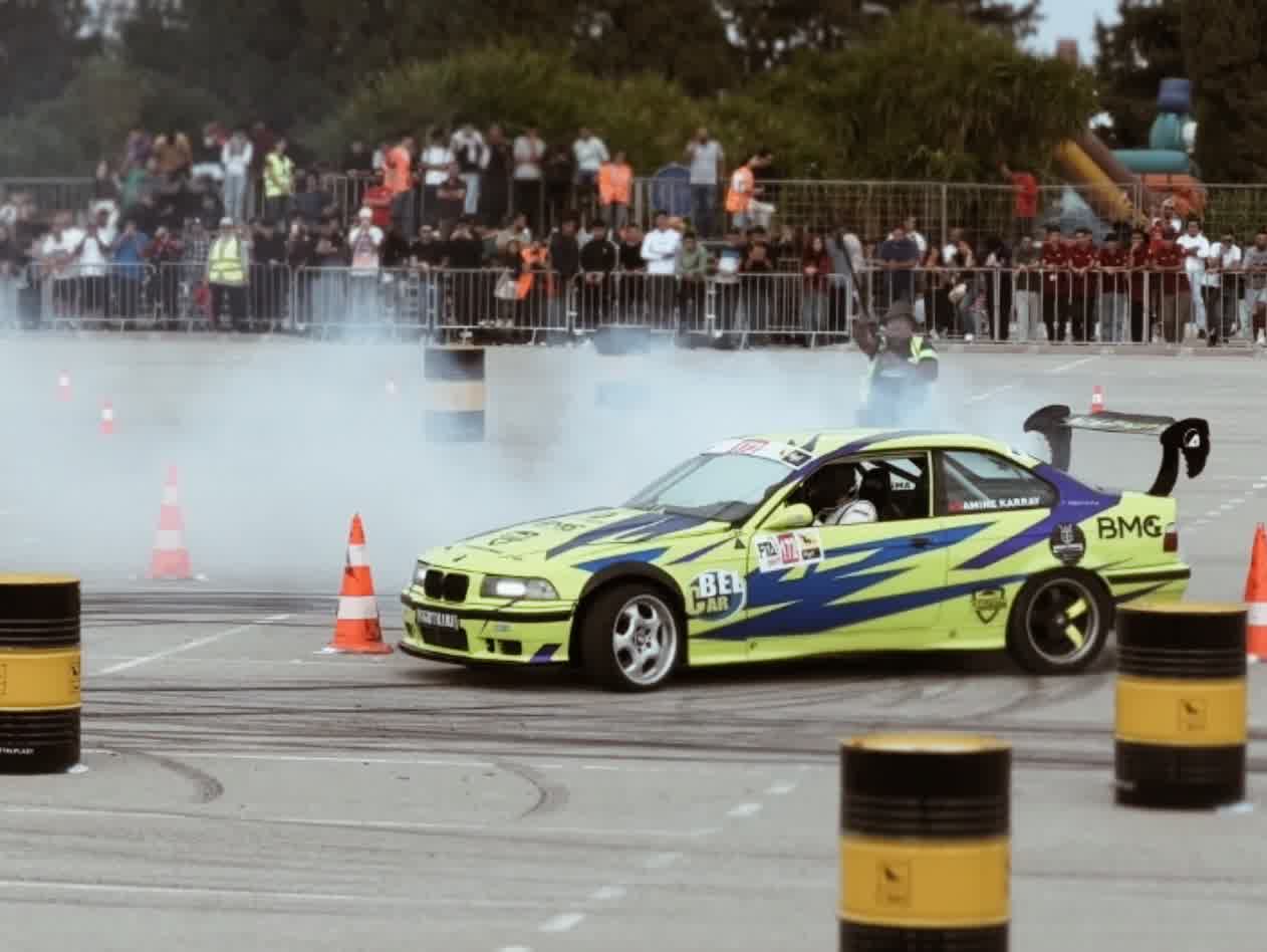 A yellow and blue liveried coupé clipping a cone, smoke rising across the spectators.