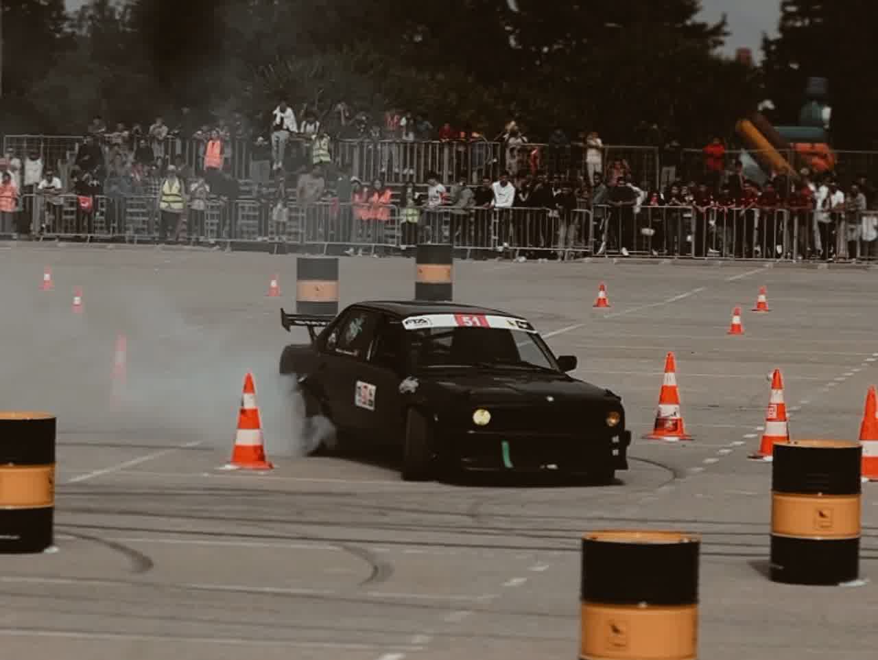 A black car threading between orange cones, the crowd watching from behind the fence.
