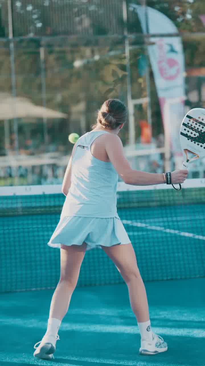 A player in white, seen from behind, striking the ball on an outdoor padel court.