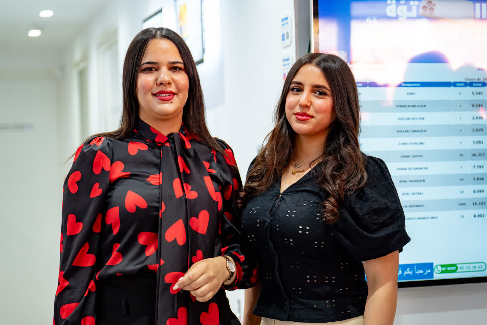 Two women standing together at an indoor event, display screens behind them.