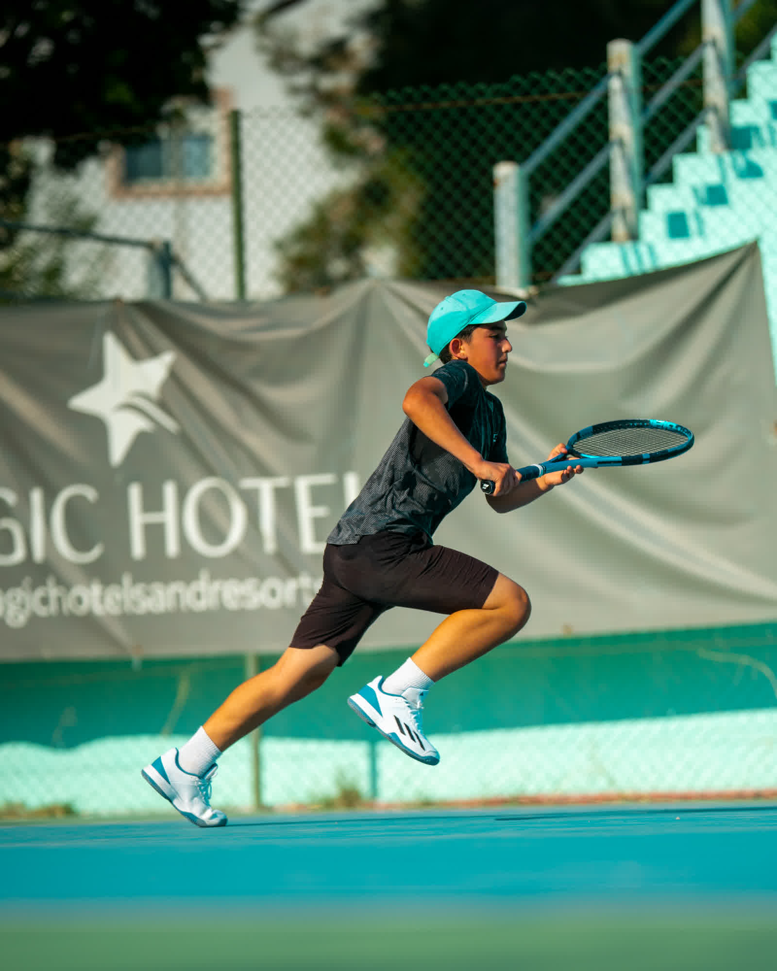 A young player leaping into a forehand, a printed banner along the fence behind.