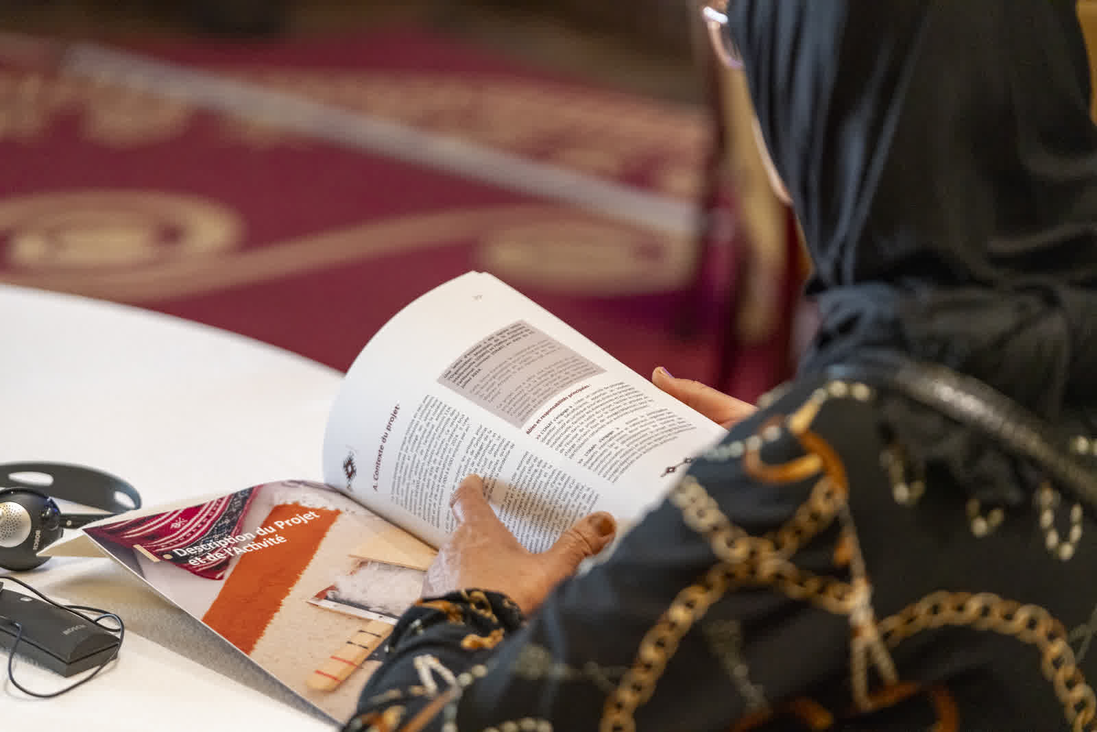 Hands turning the pages of a printed document at a table in warm light.
