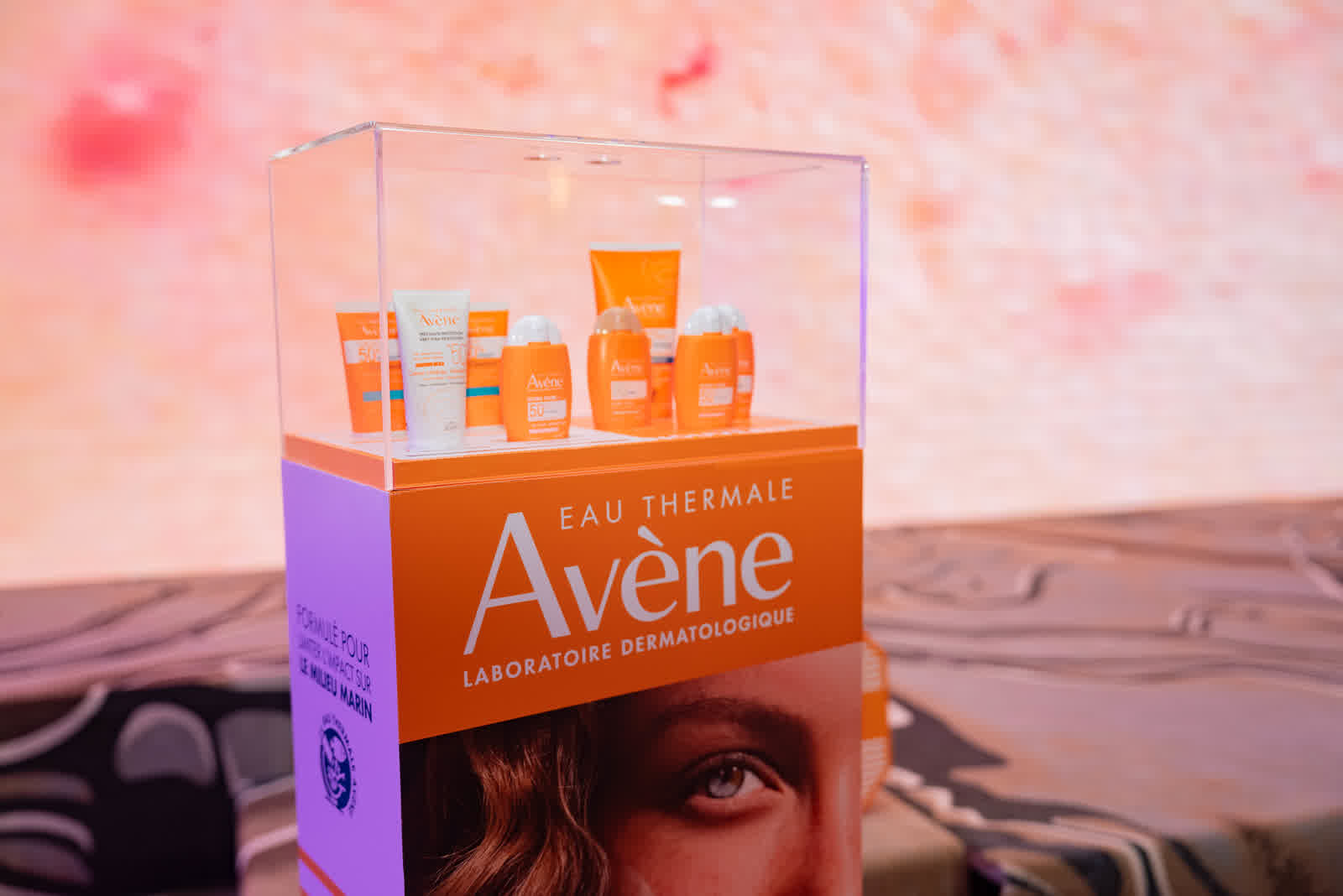 A row of skincare products displayed inside a clear case against a pink backdrop.