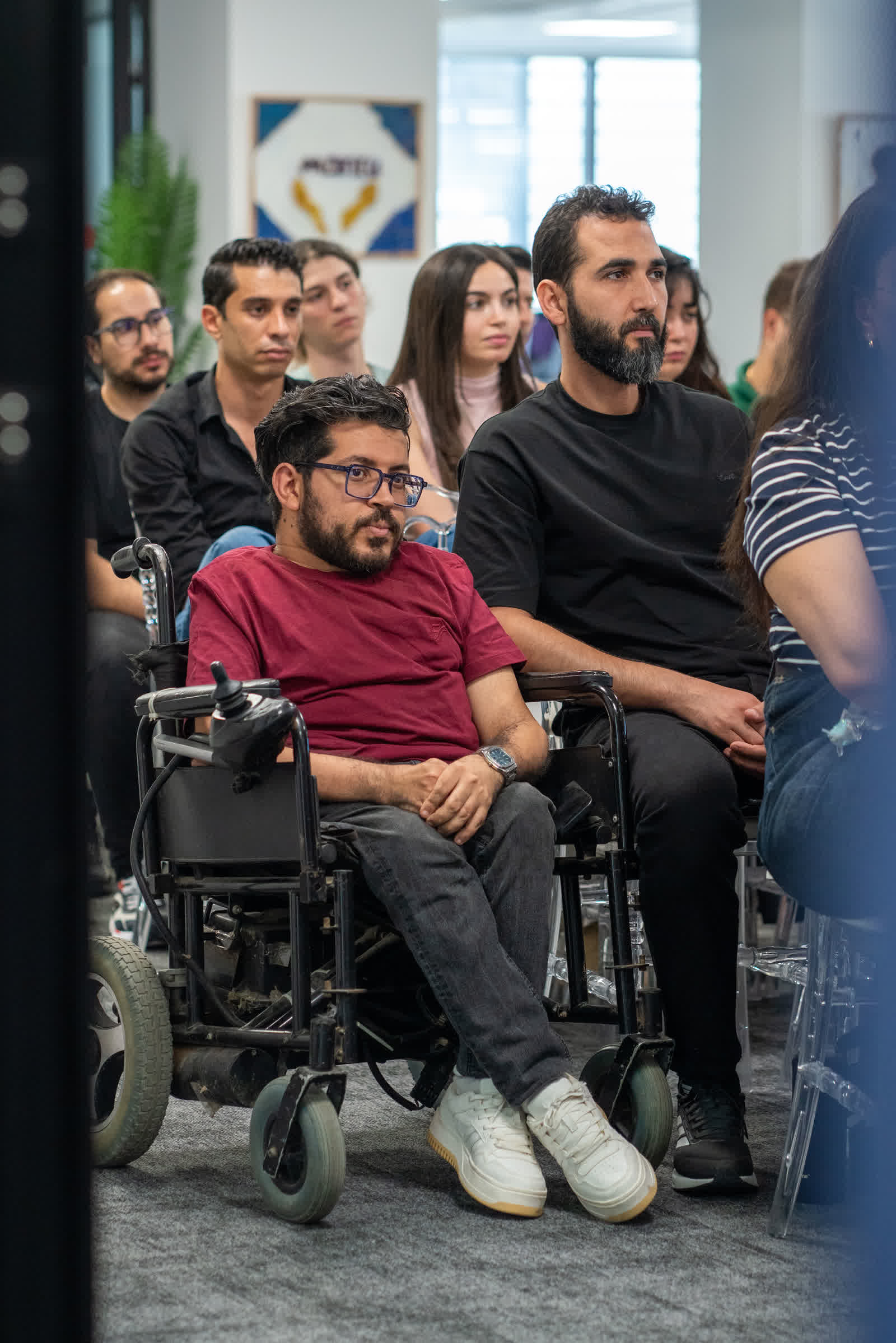 People watching a presentation, a man in a wheelchair among them in the foreground.