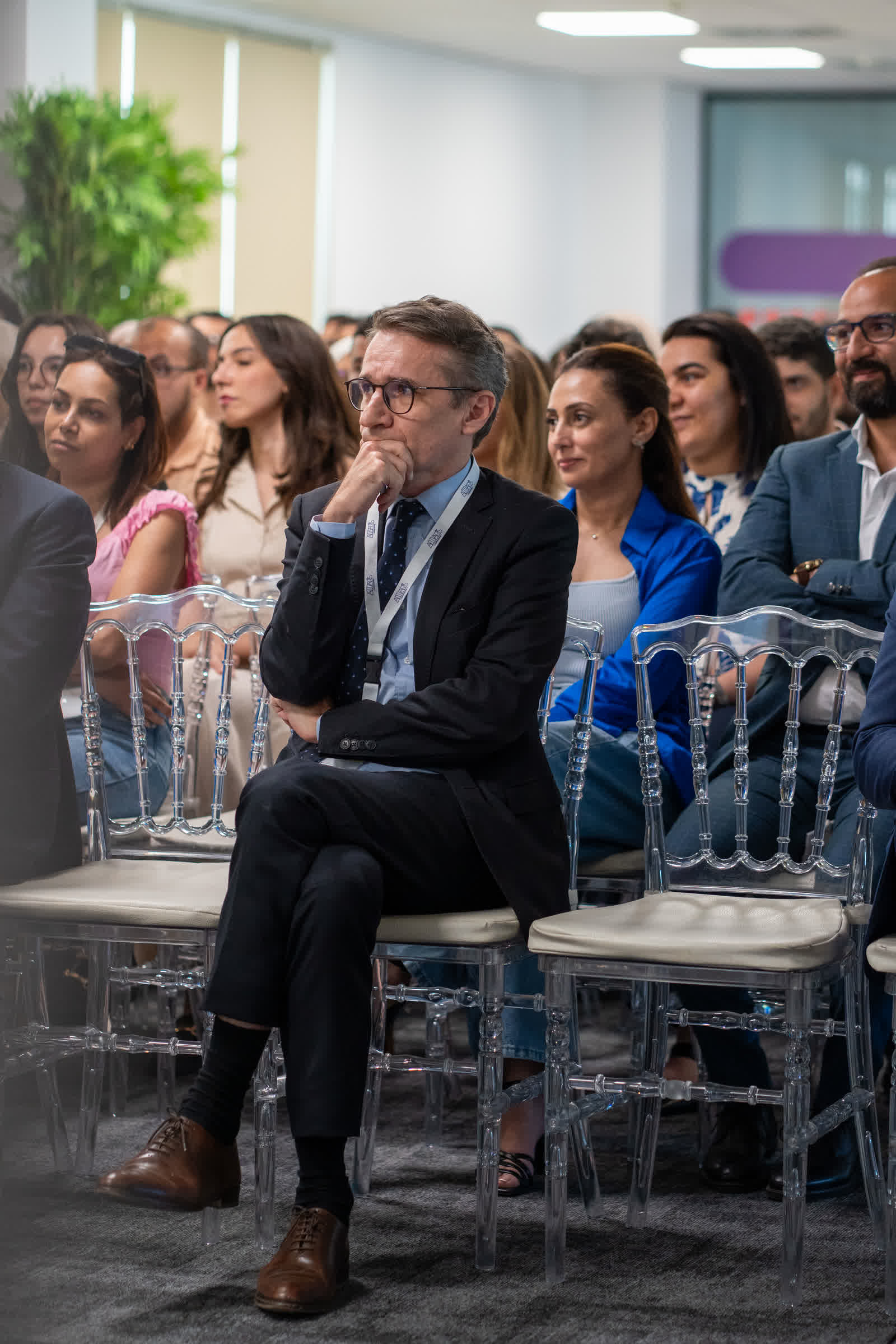 Seated guests listening at a conference, one leaning forward with his hands clasped.