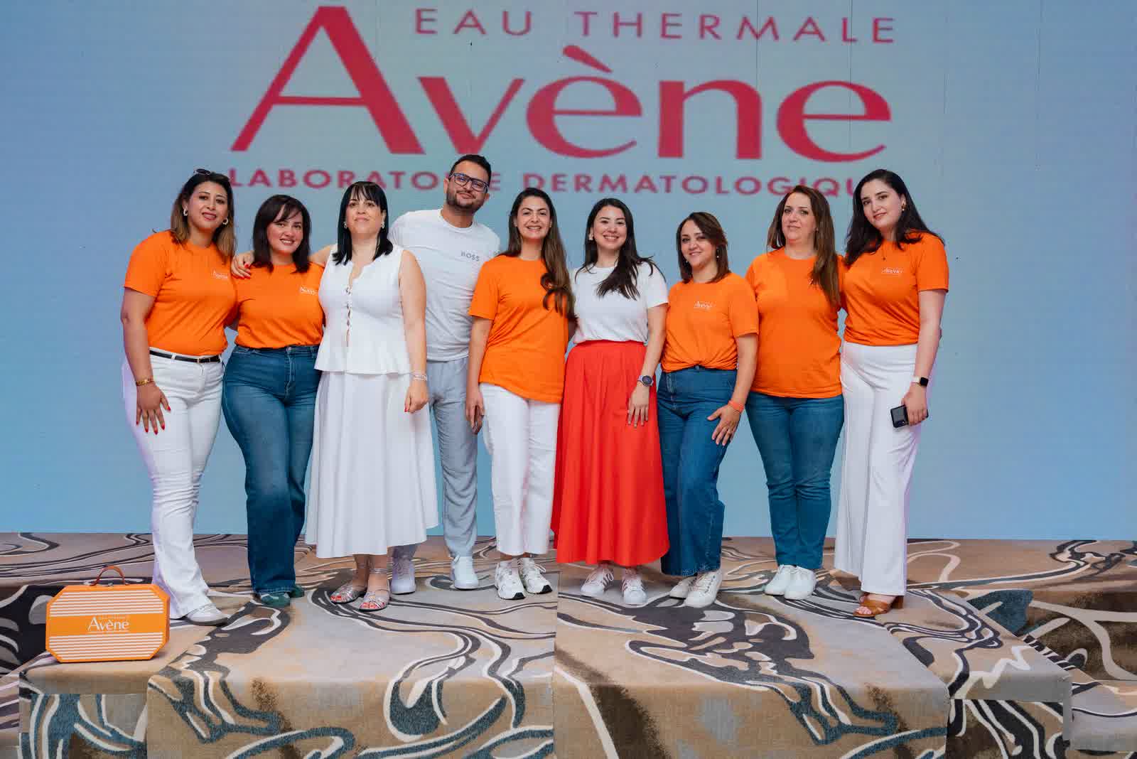 A group in orange and white standing together on stage in front of a large printed backdrop.