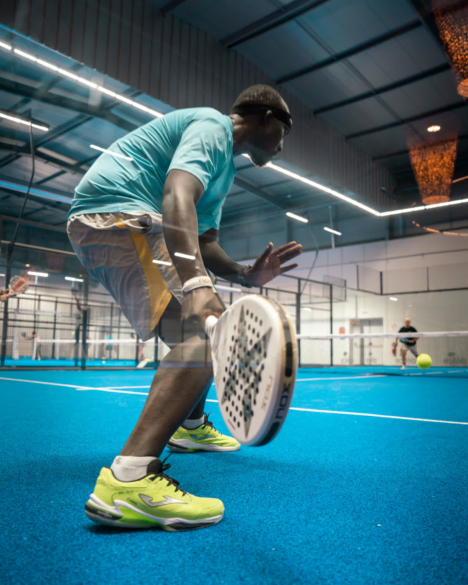 A player lunging low to reach a ball on an indoor blue court, racket stretched out.