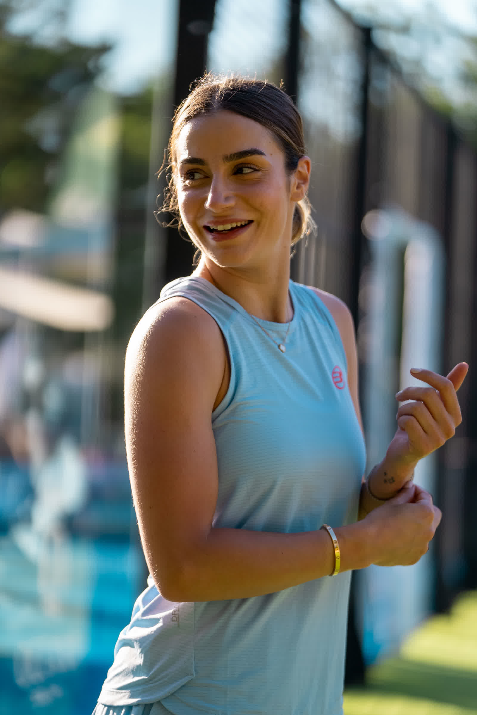 A player in a pale blue top smiling, the glass wall of the court behind her.