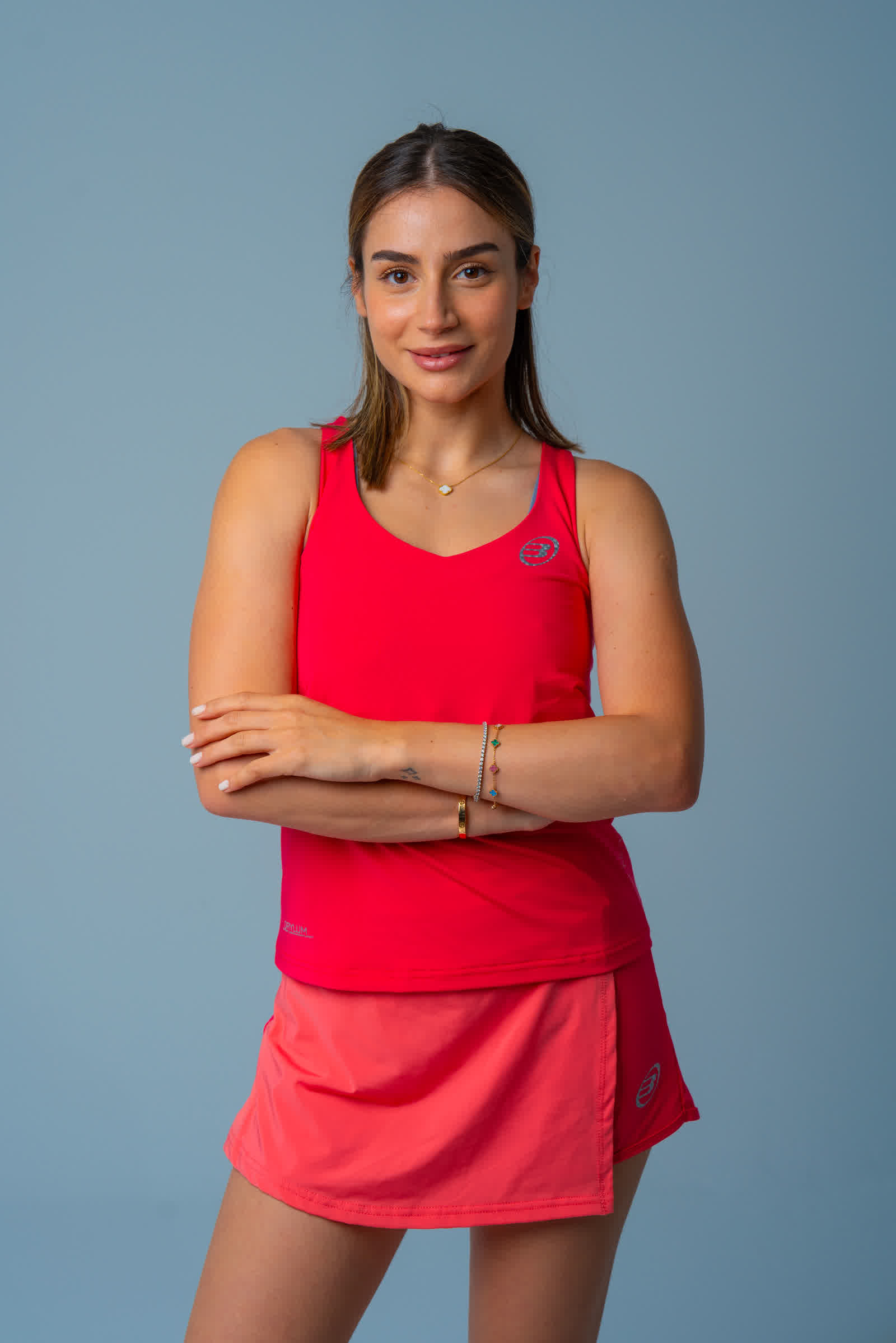 Studio portrait: a player in a red top with her arms folded, against a grey backdrop.