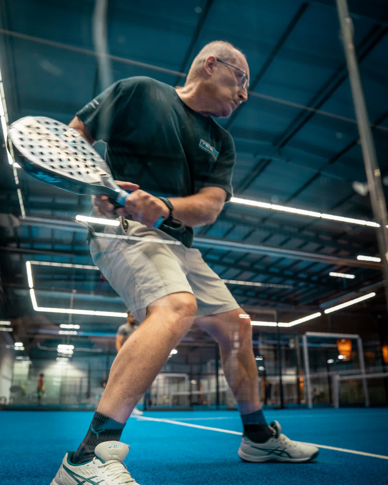 A player in a black shirt hitting a two-handed backhand on an indoor court.