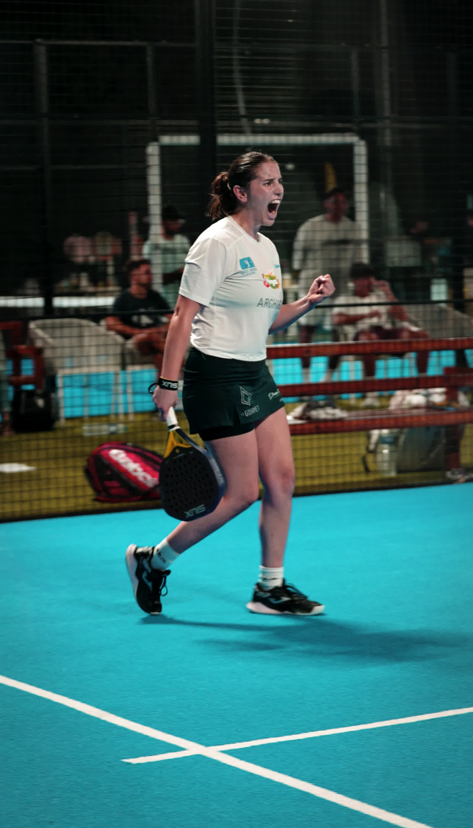 A player in white shouting in celebration on a teal court.