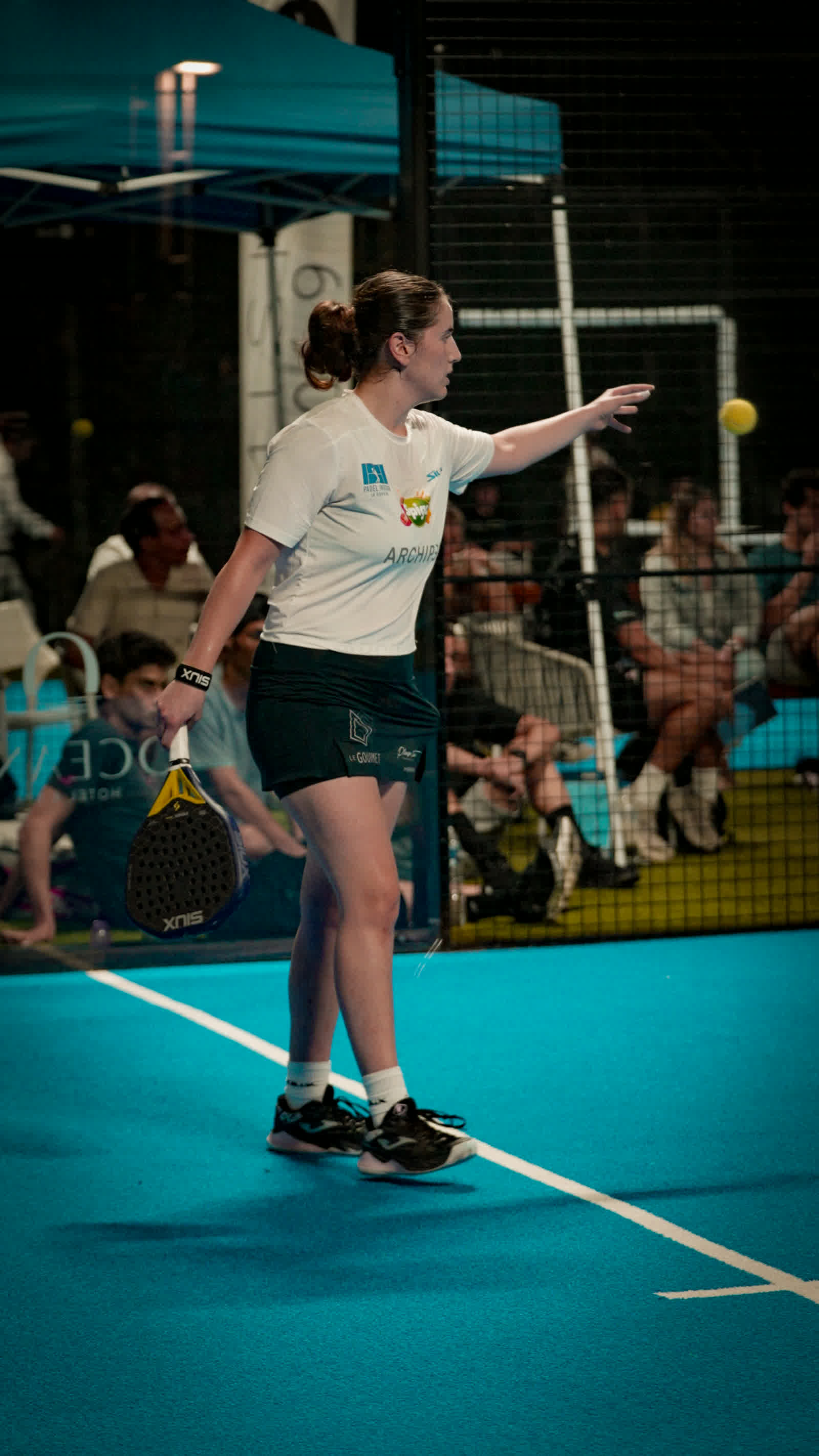 A player serving, the ball suspended in the air above her racket.